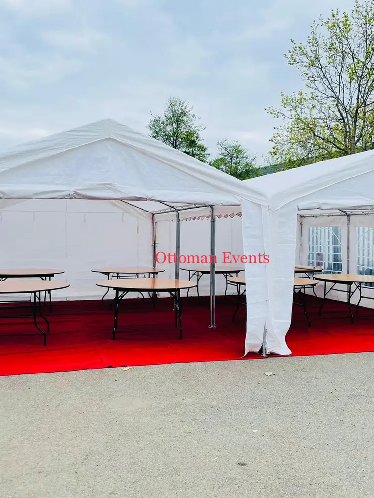 Two joined white marquees with red carpet flooring and round wooden tables