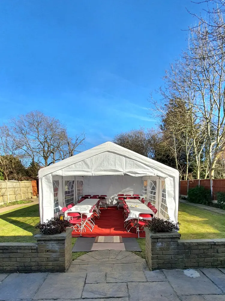 White marquee in a back garden with red chairs and red carpet under blue sky