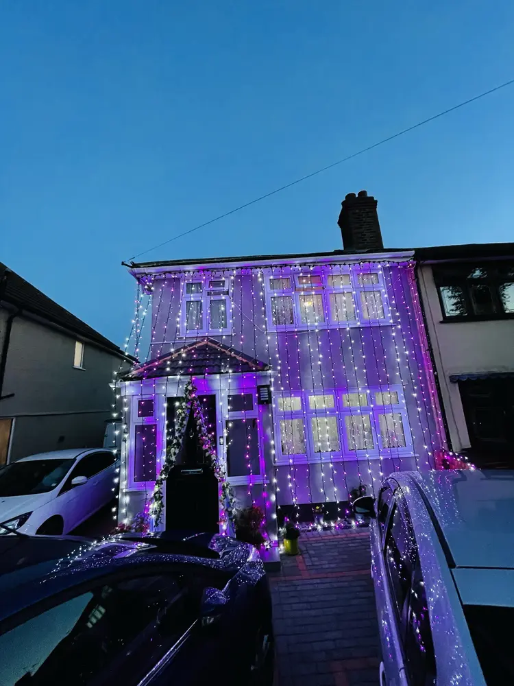 House front covered in purple and white curtain fairy lights at dusk